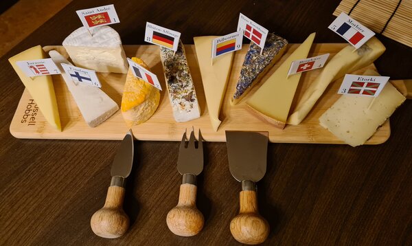 D1940_CharityCheeseTasting_5223139-g-rausch-10er-kasevariation.jpg Mehrere Käsesorten versehen mit Länderflaggen auf einem Holzbrett