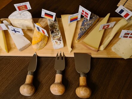 Mehrere Käsesorten versehen mit Länderflaggen auf einem Holzbrett