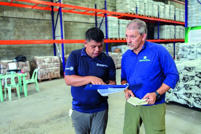 Konzentriert blicken Domi Jun Elico und Brian Glenn auf ihre Notizen. Sie haben sich genau notiert, welche Hilfsgüter in welcher Zahl heute verladen werden müssen.