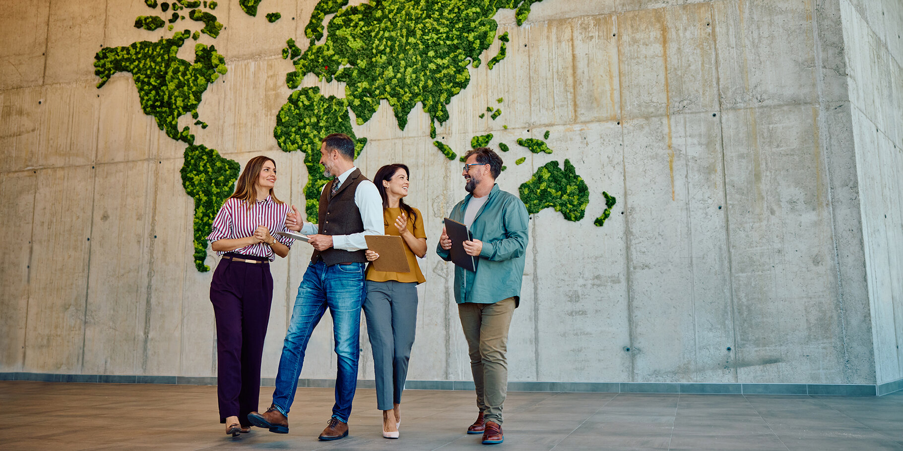 zwei Frauen und Männer stehen vor einer großen Wand wo die Kontinente aus unterschiedlichen grünen Perforationen besteht
