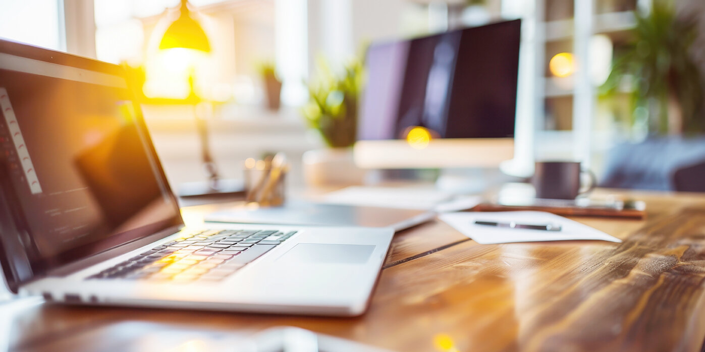 Schreibtischansicht mit einem Laptop und Bildschirm, Arbeitsplatz und Lampe im Hintergrund