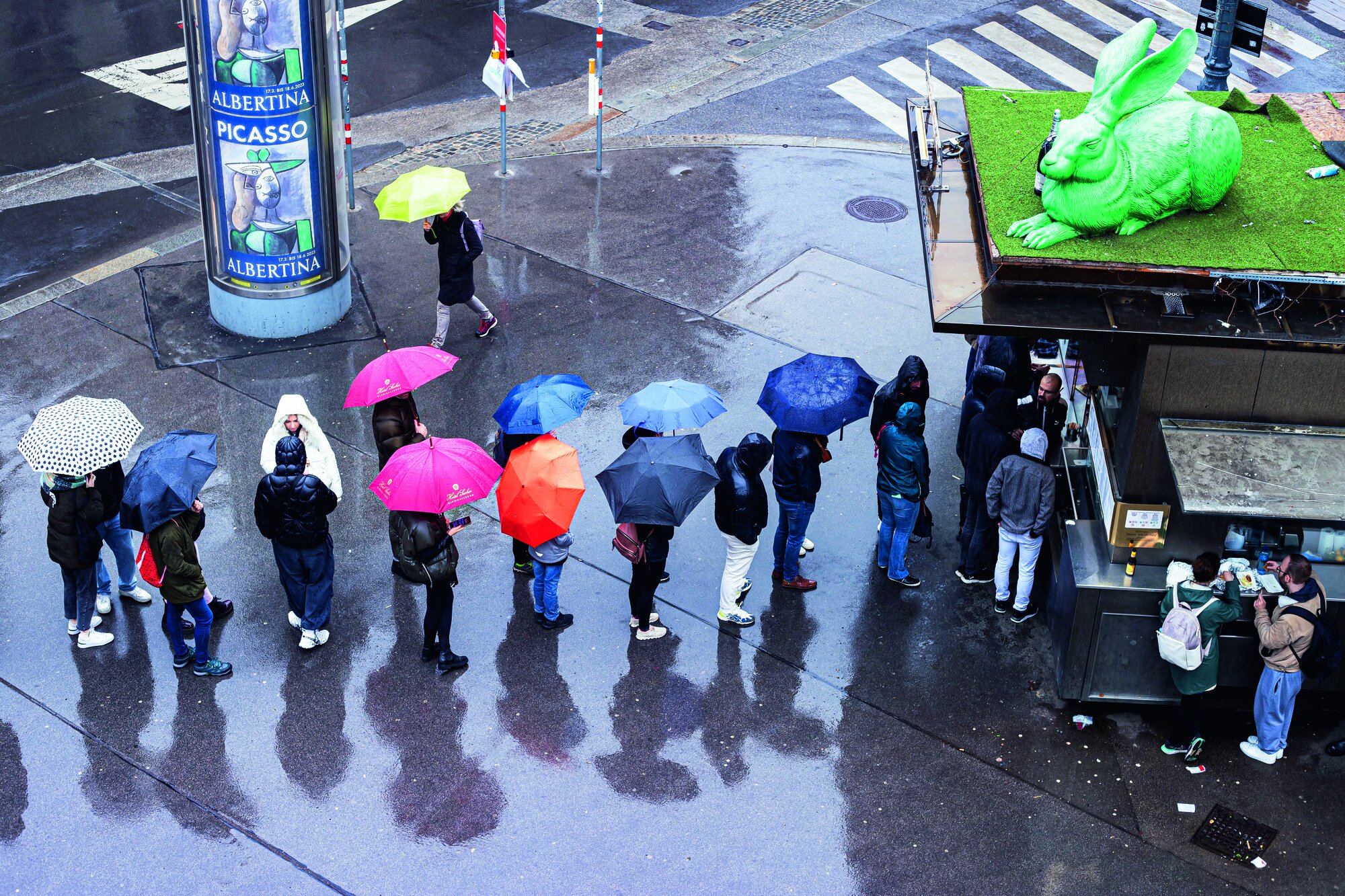 Menschen stehen bei regnerischem Wetter mit Regenschirmen in der Schlange vor dem bekannten Wiener Würstelstand Bitzinger in der Nähe der Staatsoper in Wien
