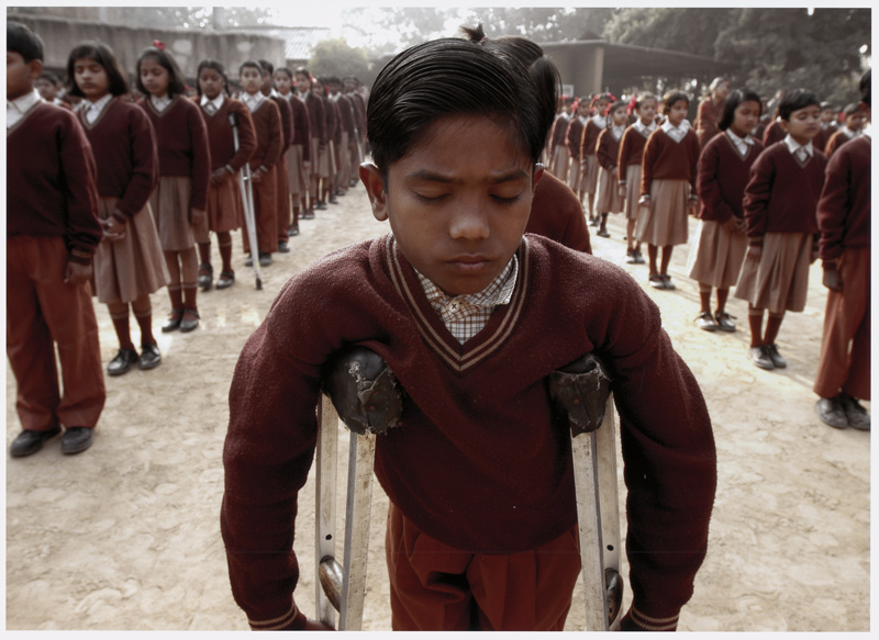 Jean-Marc-Giboux-Ausstellung, polio, Bild 4, Junge in Indien steht mit Krücken bei einer Schulversammlung